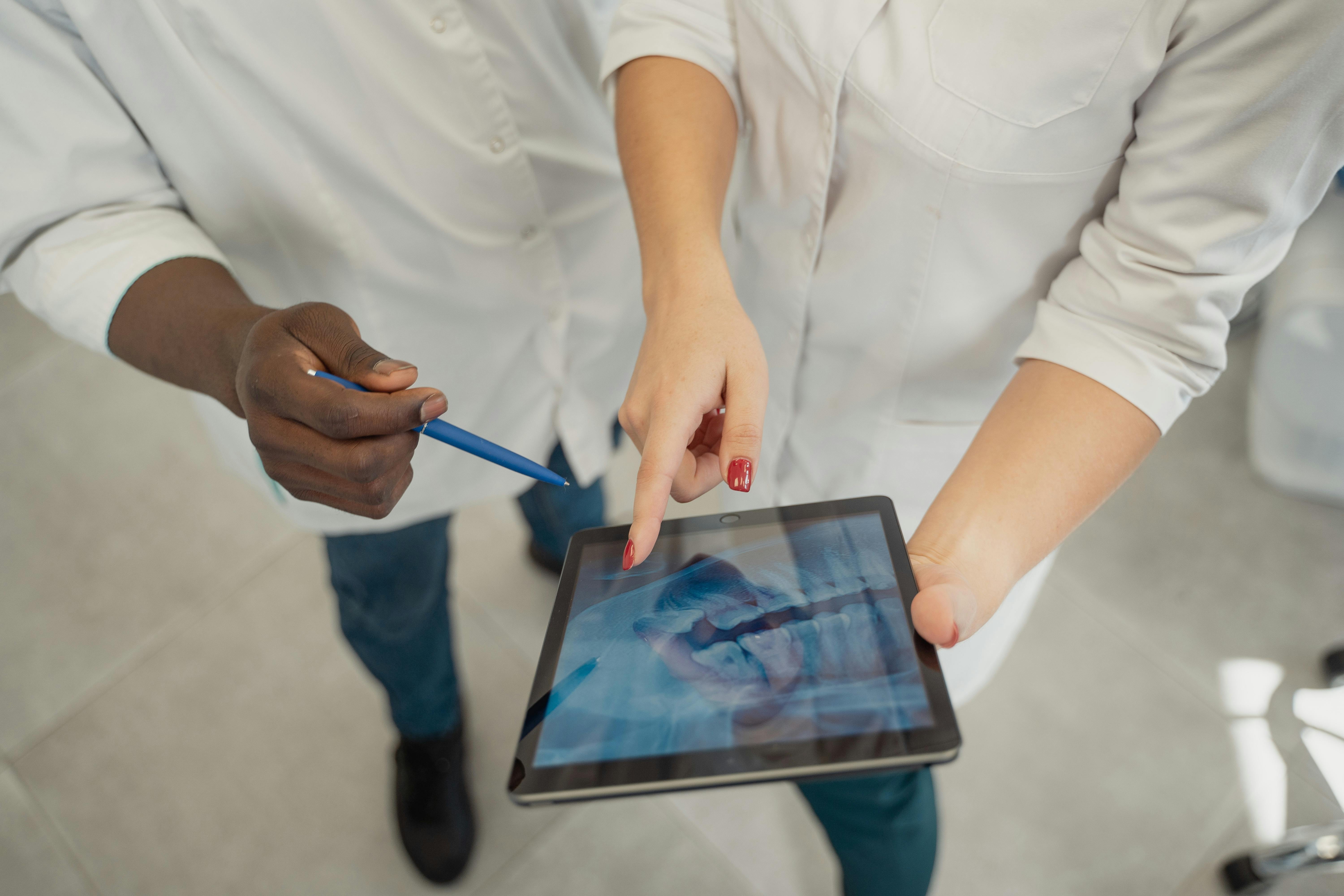 Two medical professionals at Royal Wound Care examining a dental X-ray on a tablet, discussing treatment options and patient care strategies. Two medical professionals at Royal Wound Care examining a dental X-ray on a tablet, discussing treatment options and patient care strategies.