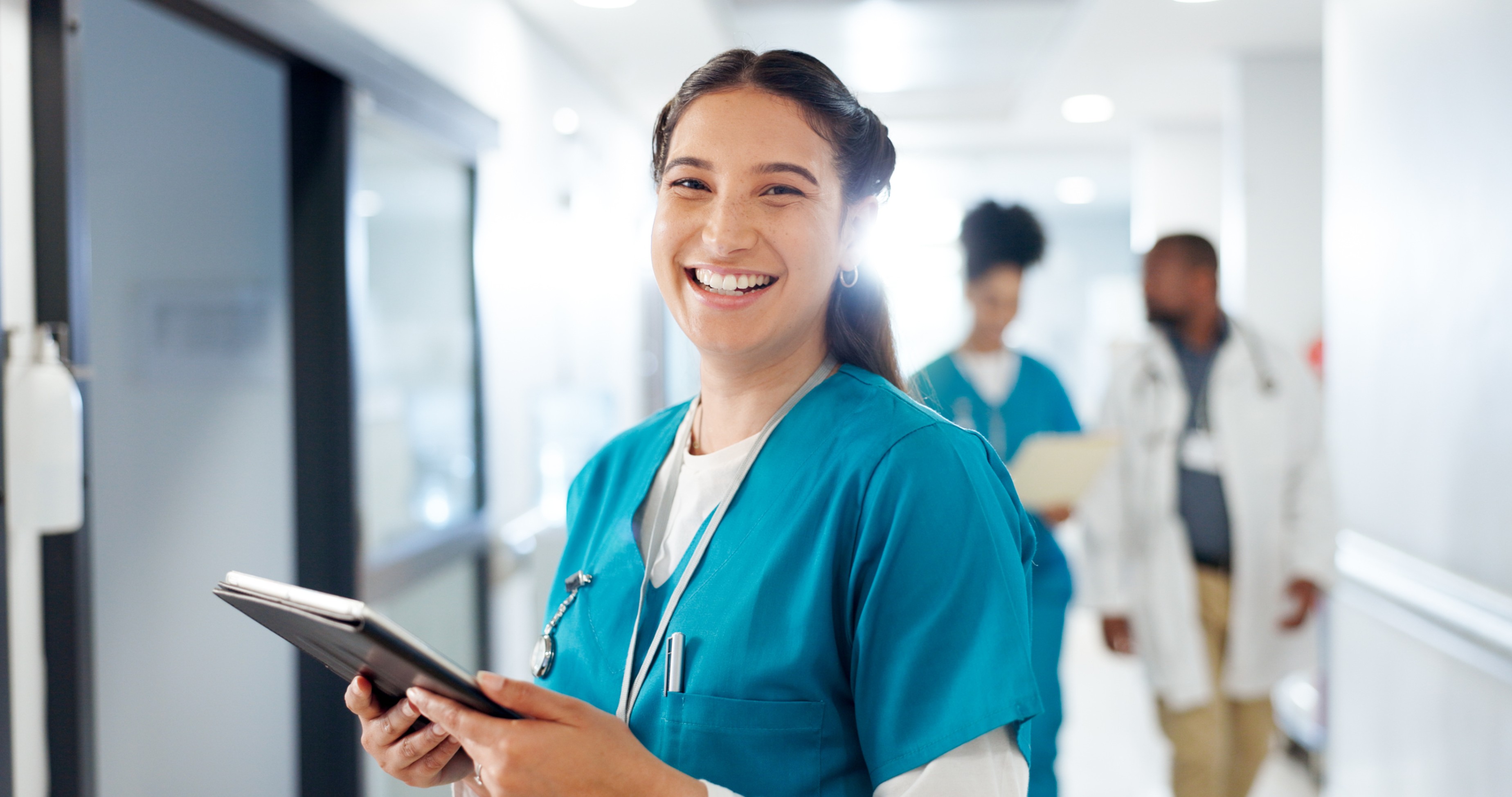 Smiling nurse in scrubs holding a tablet in a hospital hallway – Royal Wound Care’s dedicated clinical team committed to exceptional patient care and wound healing.
